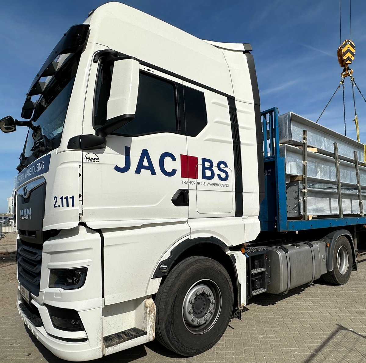 White Jacobs flatbed truck being loaded by a crane